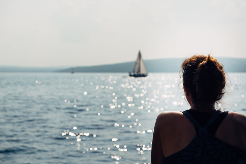 Person looking at a bay with a sailboat visible in distance